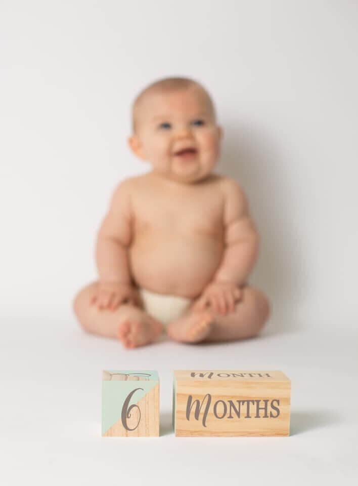 A cute baby sites on front of blacks that says 6 months old.
