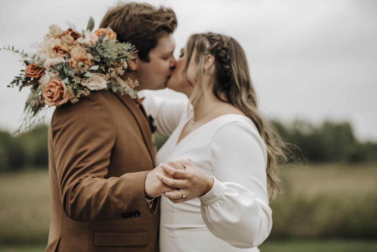 A tender moment as a newlywed couple shares a kiss, with the bride holding a beautiful bouquet and the groom in a stylish brown suit taken by jen jarmuzek photography a minneapolis wedding photographer