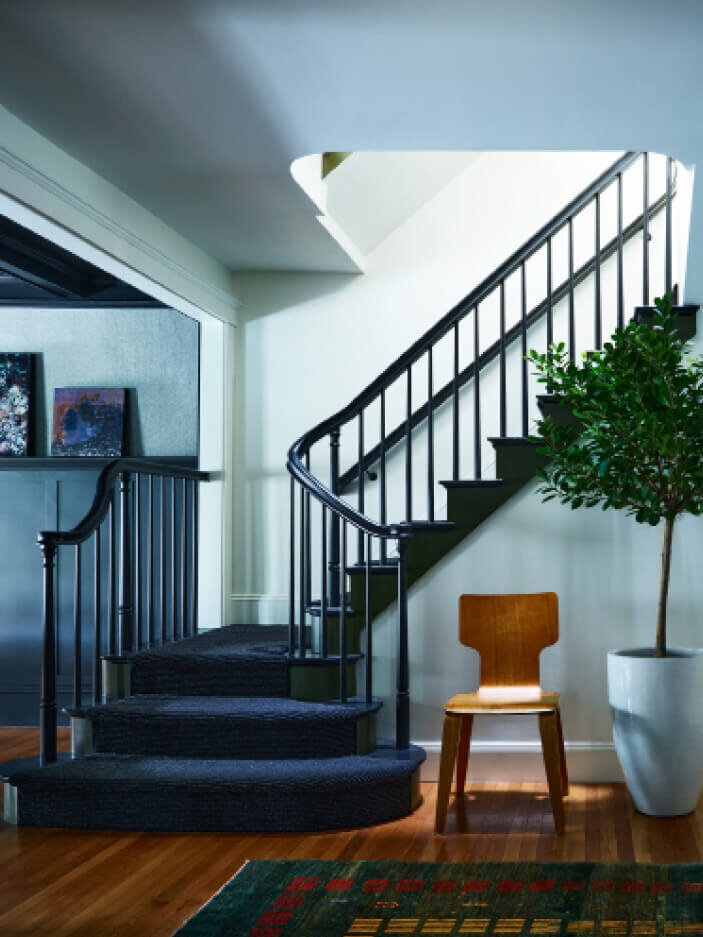 Interior designer Boston MA painted a classic stair green with a black runner, pairing it with mid-century modern-inspired furniture for a bold, timeless look.