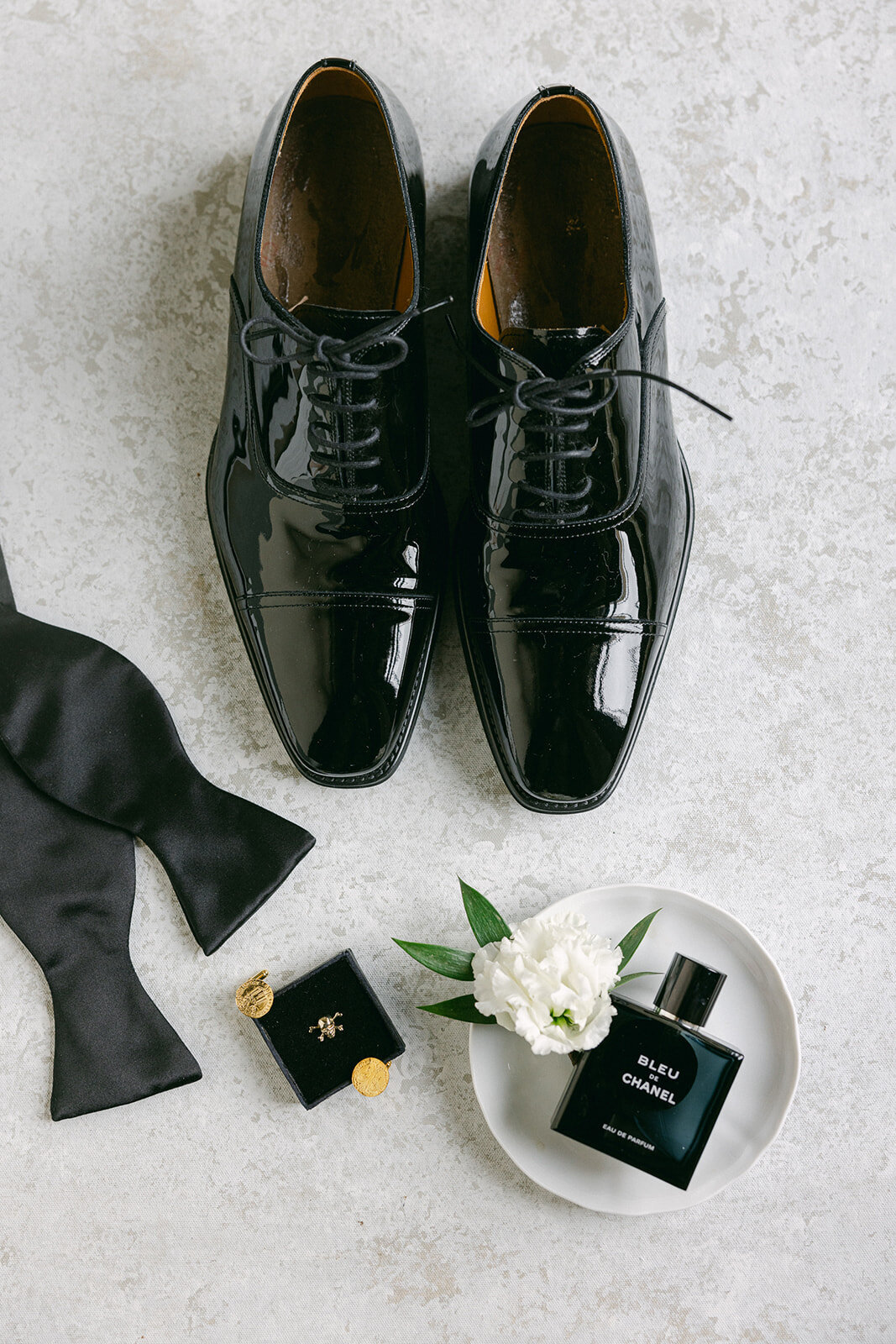 flat lay of a groom's dress shoes, tie, and wedding ring