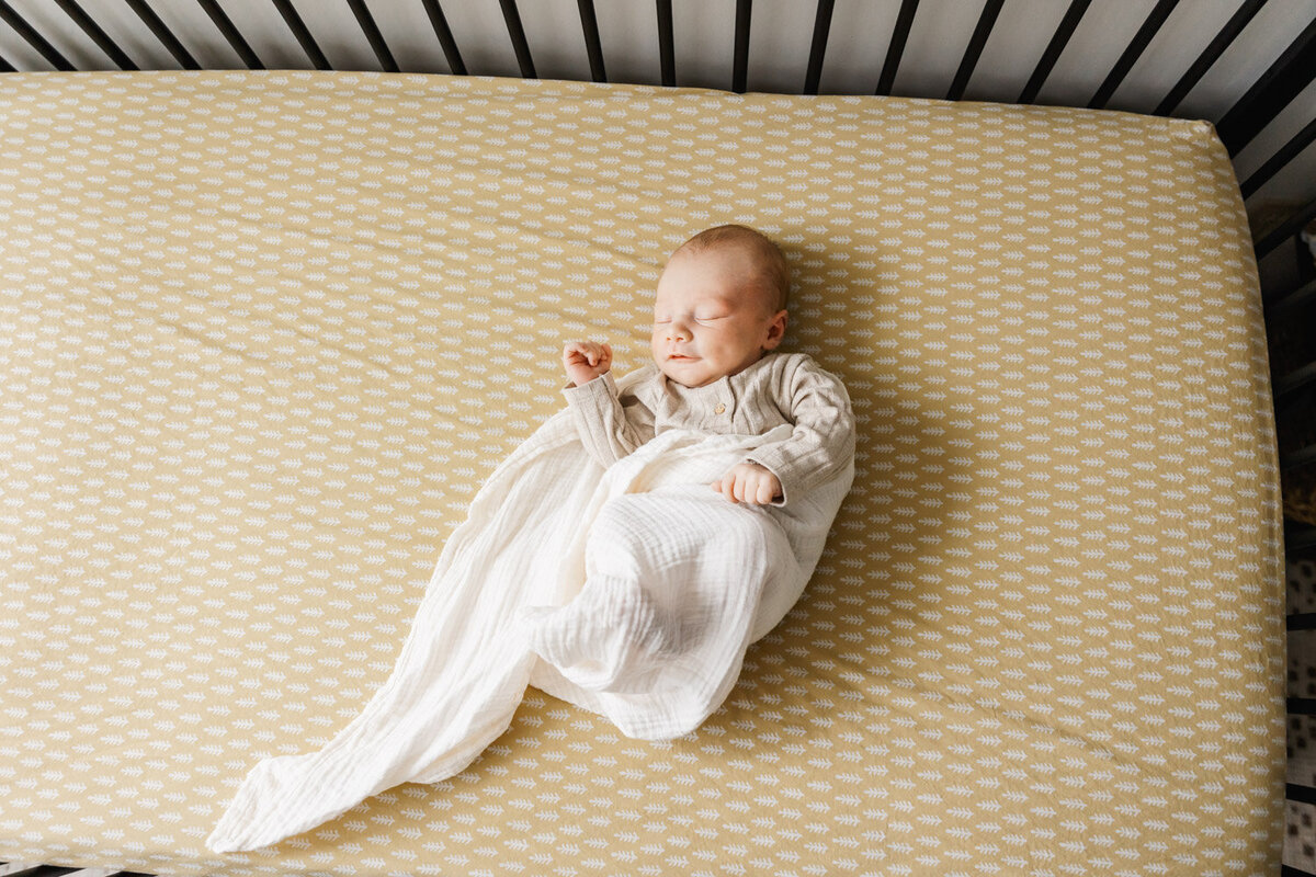 baby boy in creme swaddle laying in crib with bright sunny sheet