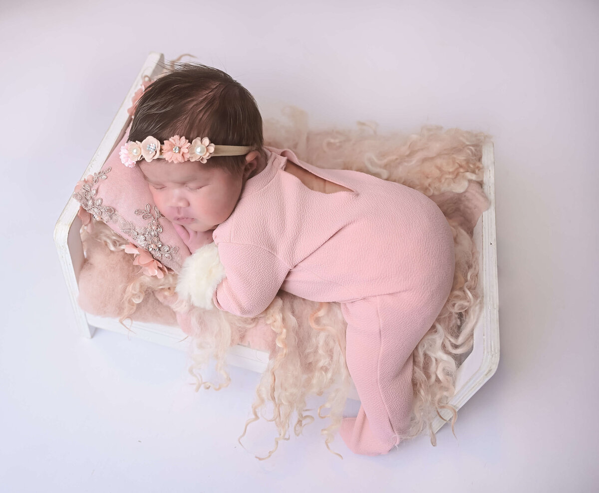 Newborn photo session where baby is dressed in pink and posed sleeping on a small white bed. Image captured by Kitsap Peninsula  photographer Beth Benecki of E. Benecki Photography.