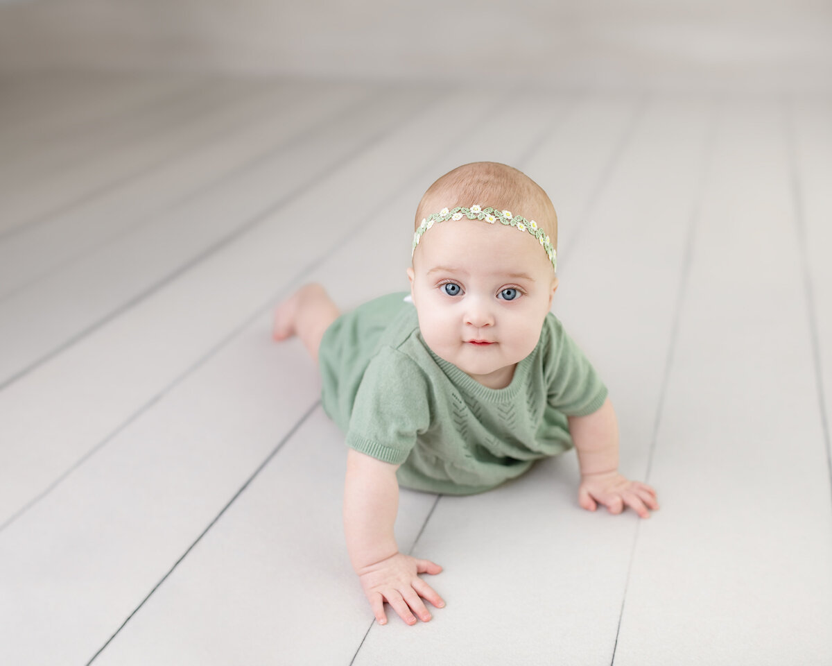 Crawling baby girl in soft green dress—captured in motion on bright white studio floors during her milestone session.