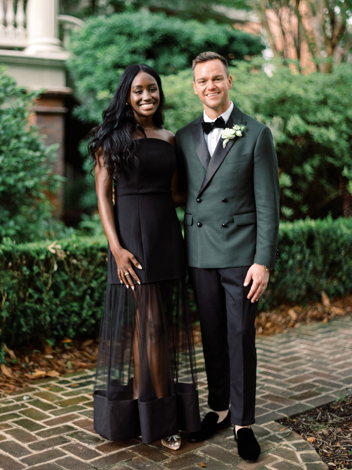 The groom stands proud beside a guest in an elegant setting, highlighting style and sophistication amid lush greenery, making for a charming wedding photograph.
