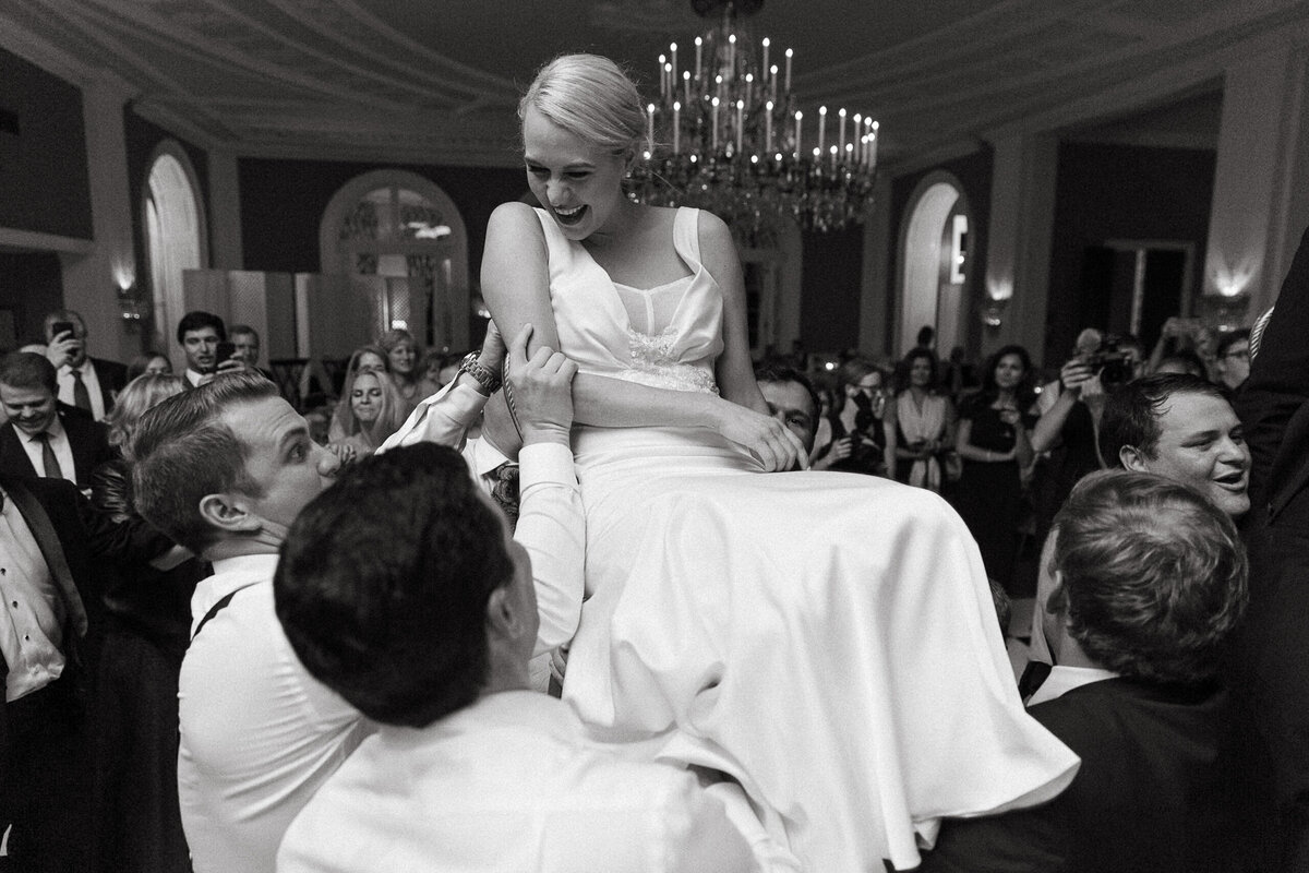 Black and white photo of a bride being held up on a chair for the hora.
