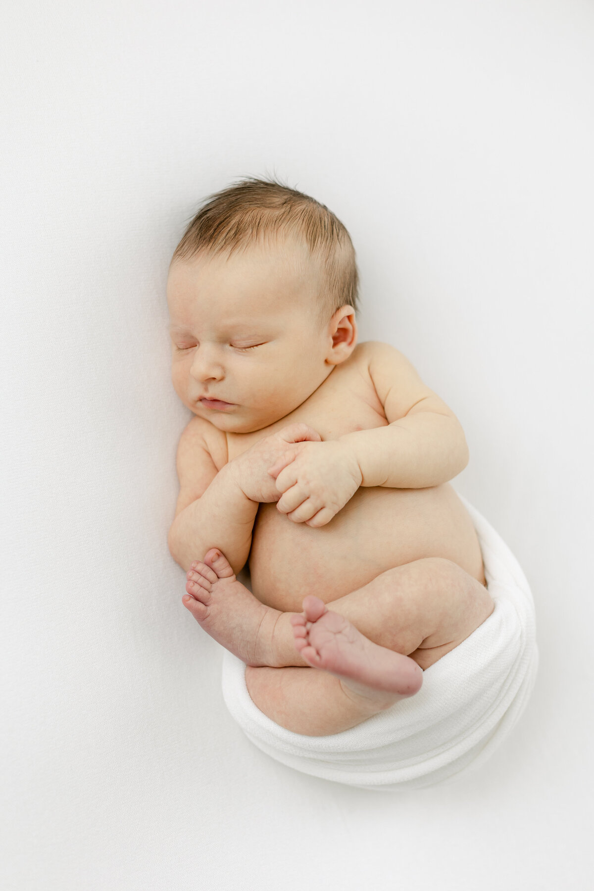 infant baby delicately swaddled in a white blanket showing his arms, belly and legs photographed by Philadelphia Newborn Photographer Tara Federico