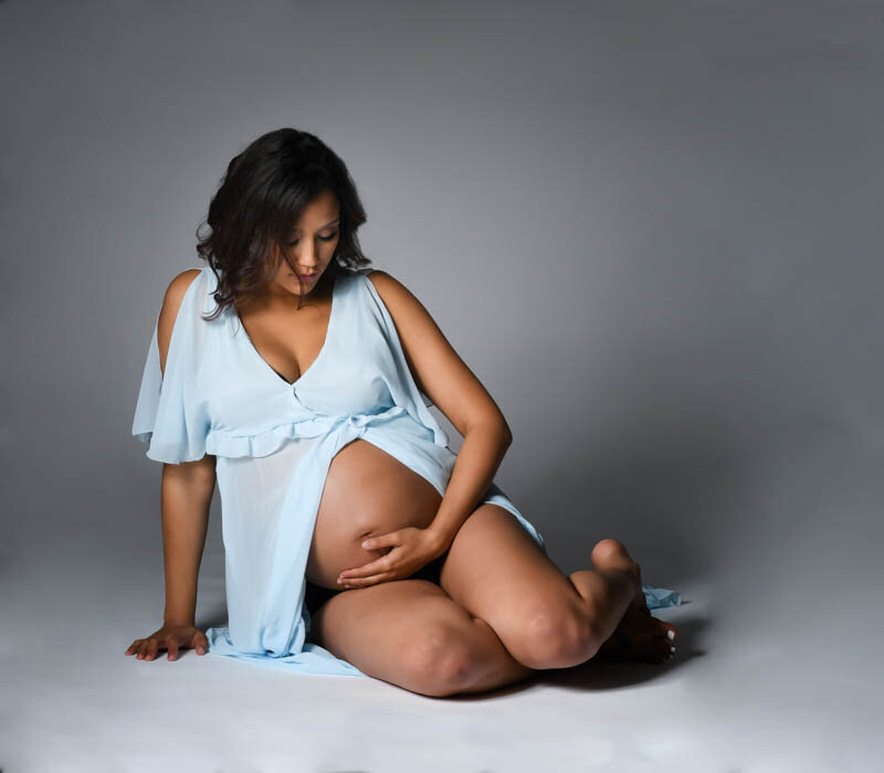 Maturnity photo of a woman in a blue gown showing her pregnant belly