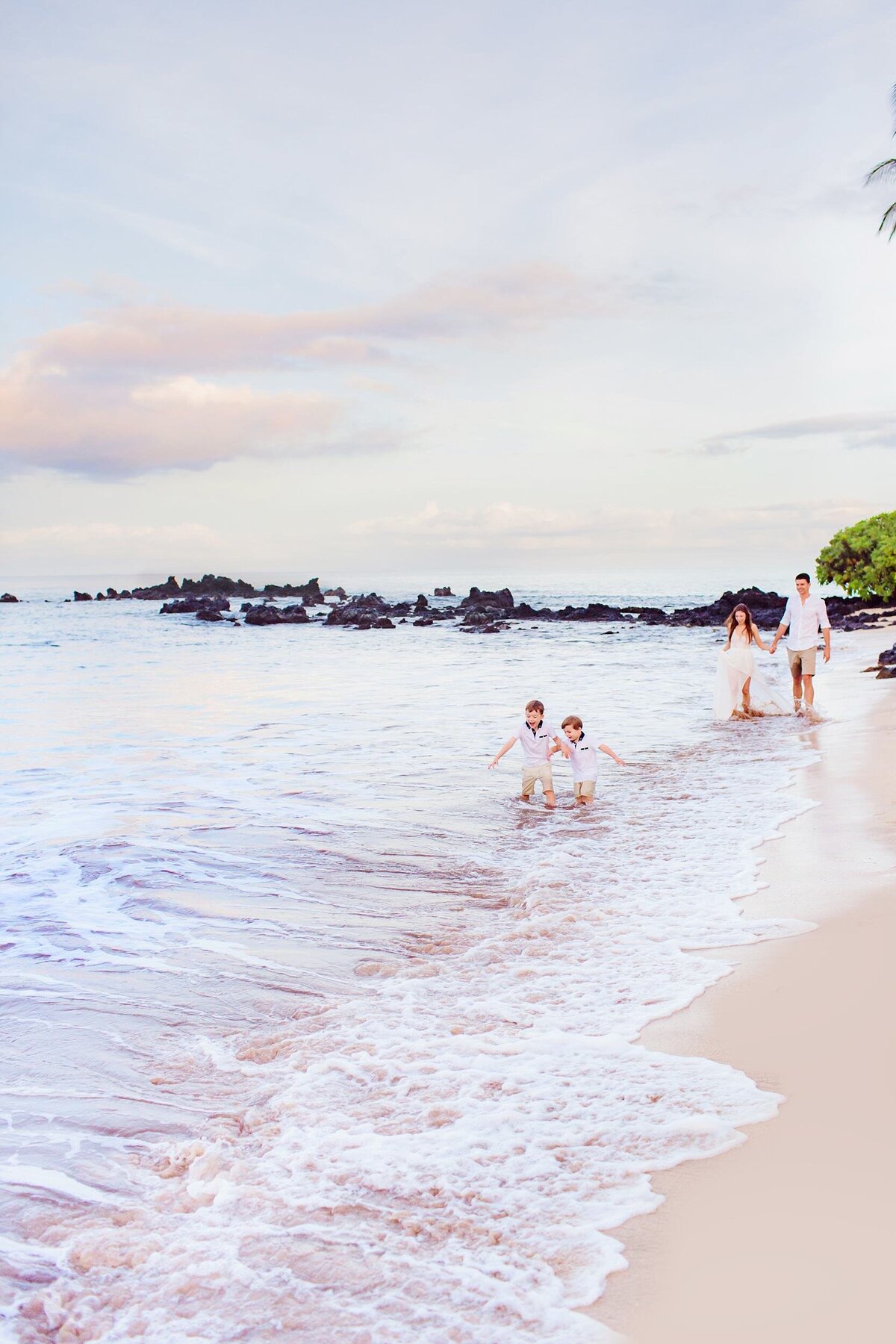 Couple walking on White Rock Beach in Wailea during their family photoshoot as two kids run ahead of them in the sand