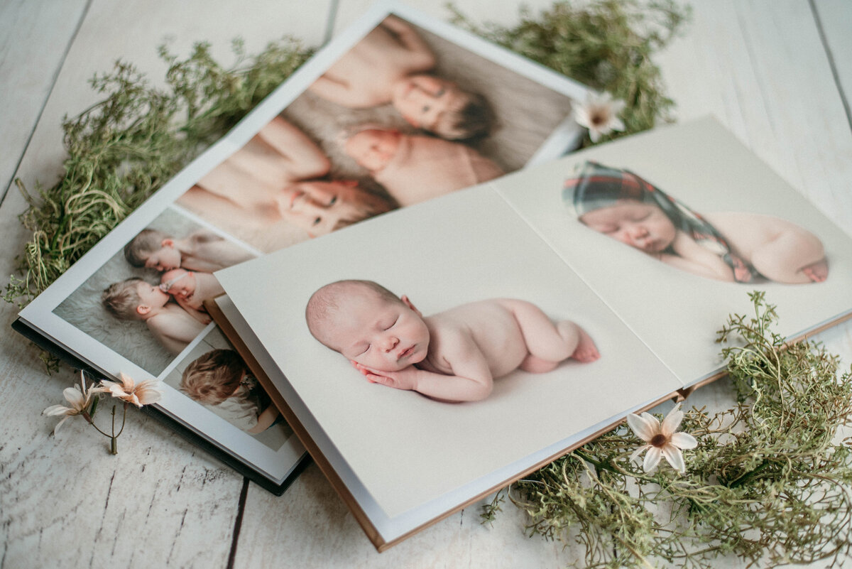 Two high end photo albums opened up to display pages showing imagery from newborn photo shoot