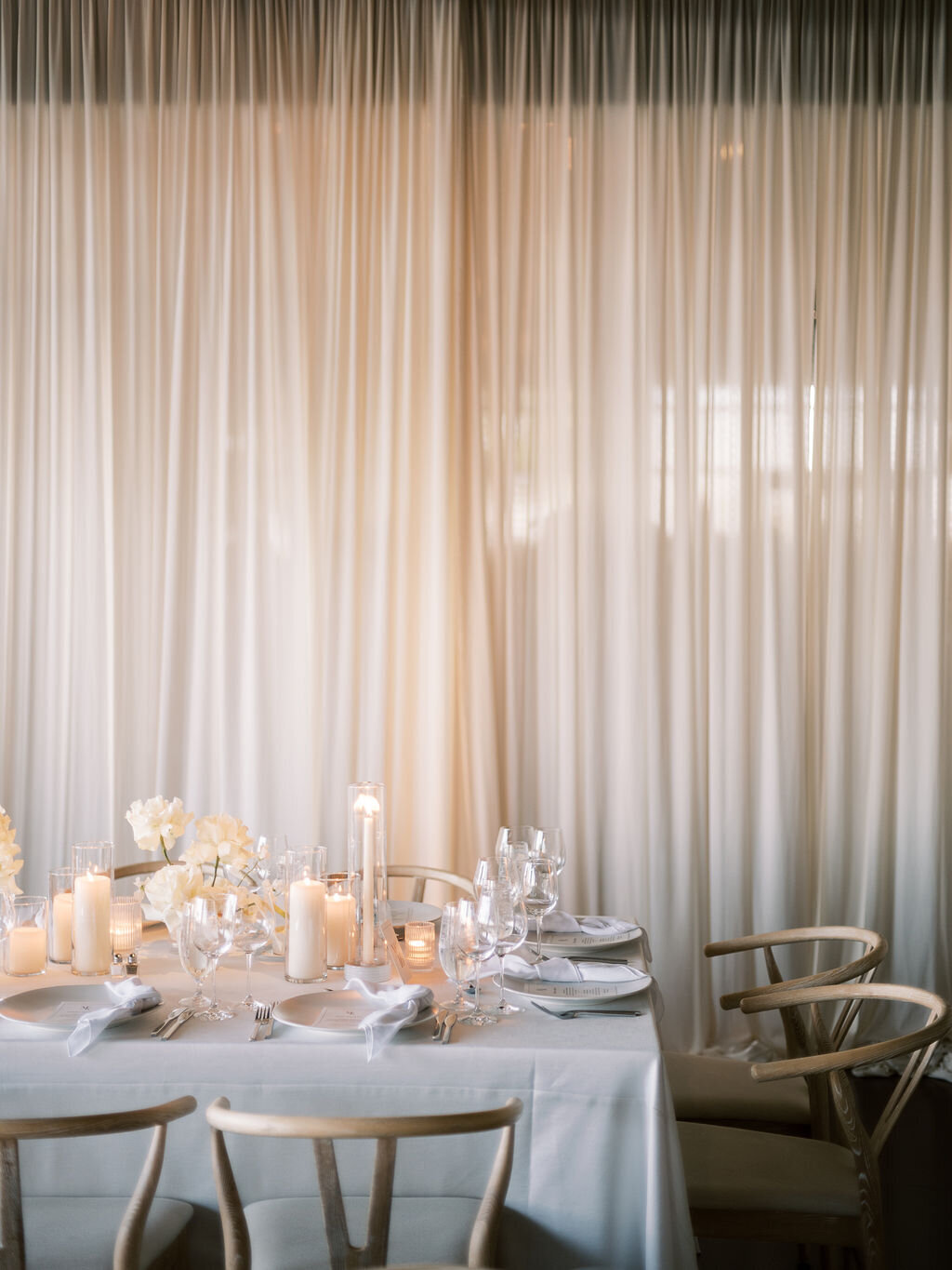 A softly lit wedding reception table with glowing candles, delicate white florals, and elegant gold-accented tableware.