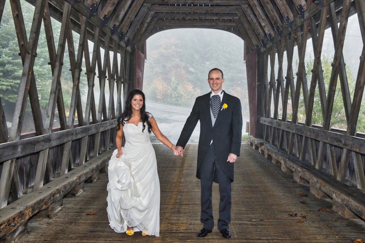 bride and groom standing underneath a covered bridge in Vermont at their Stratton Resort wedding in the fall