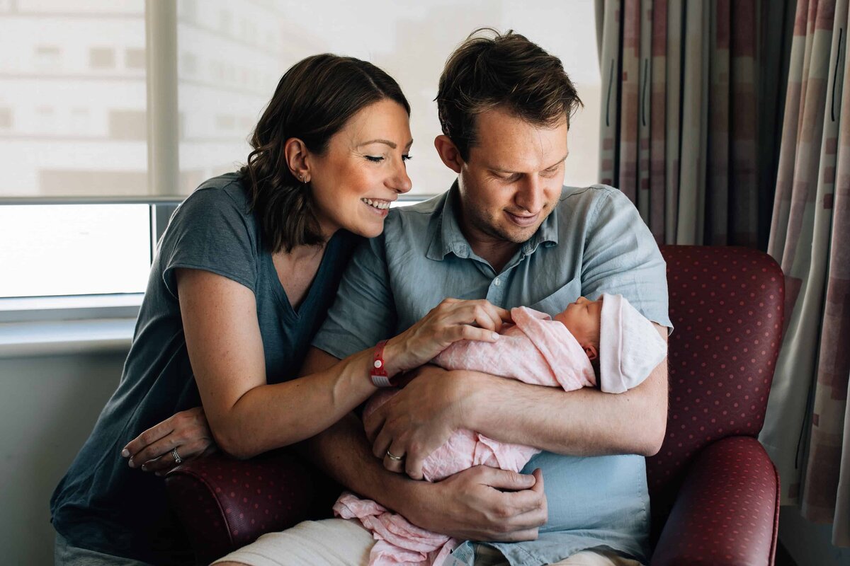 Dad holding baby with Mum looking on, Newborn Photoshoot Gift Vouchers Melbourne