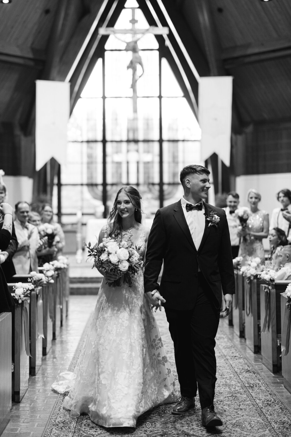 A classic black-and-white capture of the bride and groom’s joyful walk down the aisle after their vows, celebrating their first moments as newlyweds, beautifully documented on film by Morgan Alysse, Louisiana film photographer.