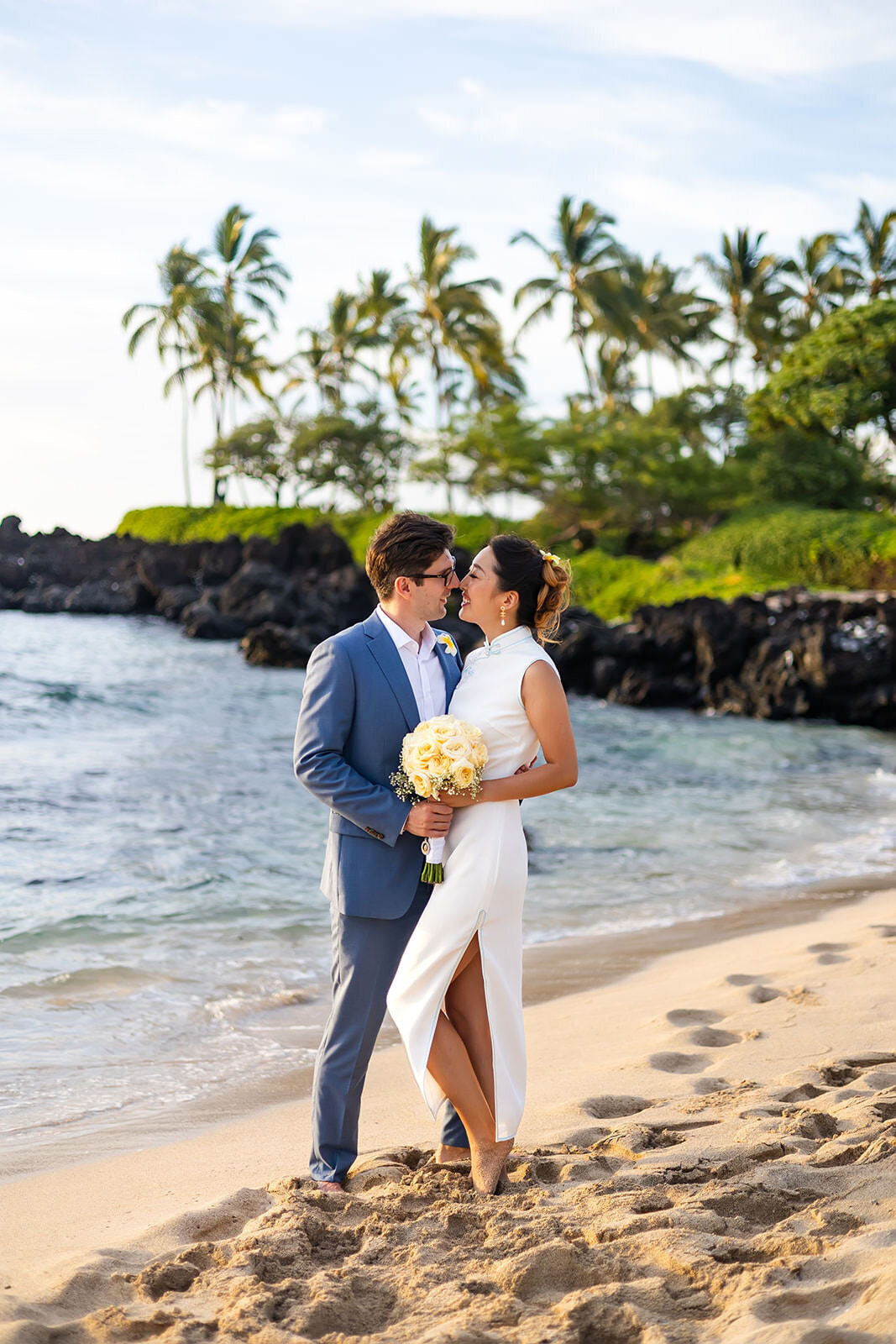 newlywed couple kissing on the beach with white dress and blue suit