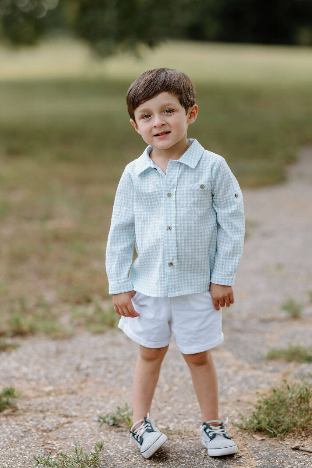 little boy in light blue and white paid shirt and white shorts smiling in East Teas field