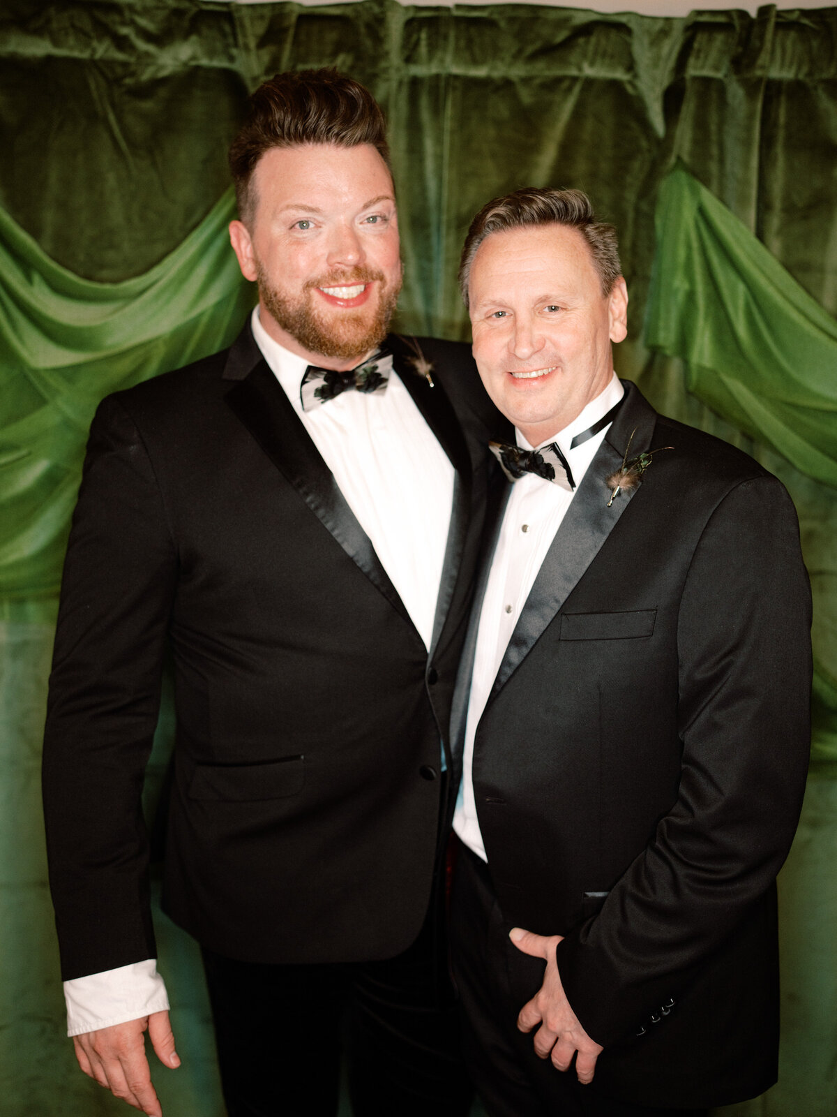 Two dapper men pose stylishly in their formal attire, exuding confidence and charm at a lively event, showcasing friendship and the joy of celebration.