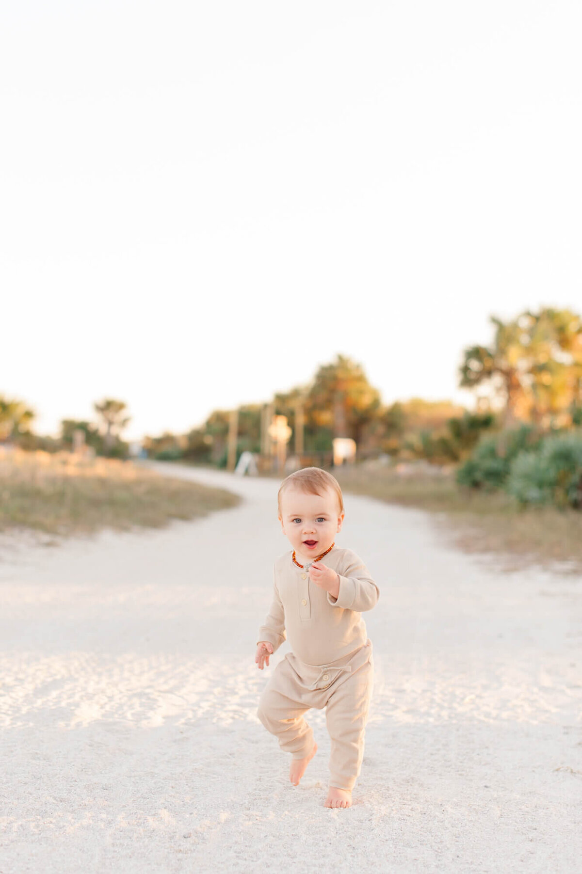 Young toddler boy walking down beach path at sunset