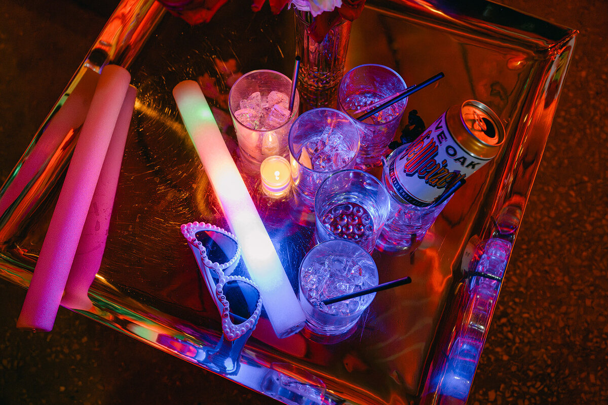 A colorful tray of glow sticks, cocktail glasses, and drinks lit under vibrant lighting—capturing the fun afterparty vibes of a high-end wedding at The Battalion in downtown San Antonio.

