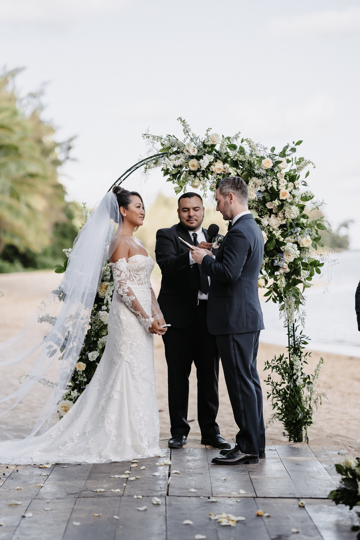 Bride and groom ceremony at Kualoa Ranch on the beach, holding hands with palm trees and ocean in the background