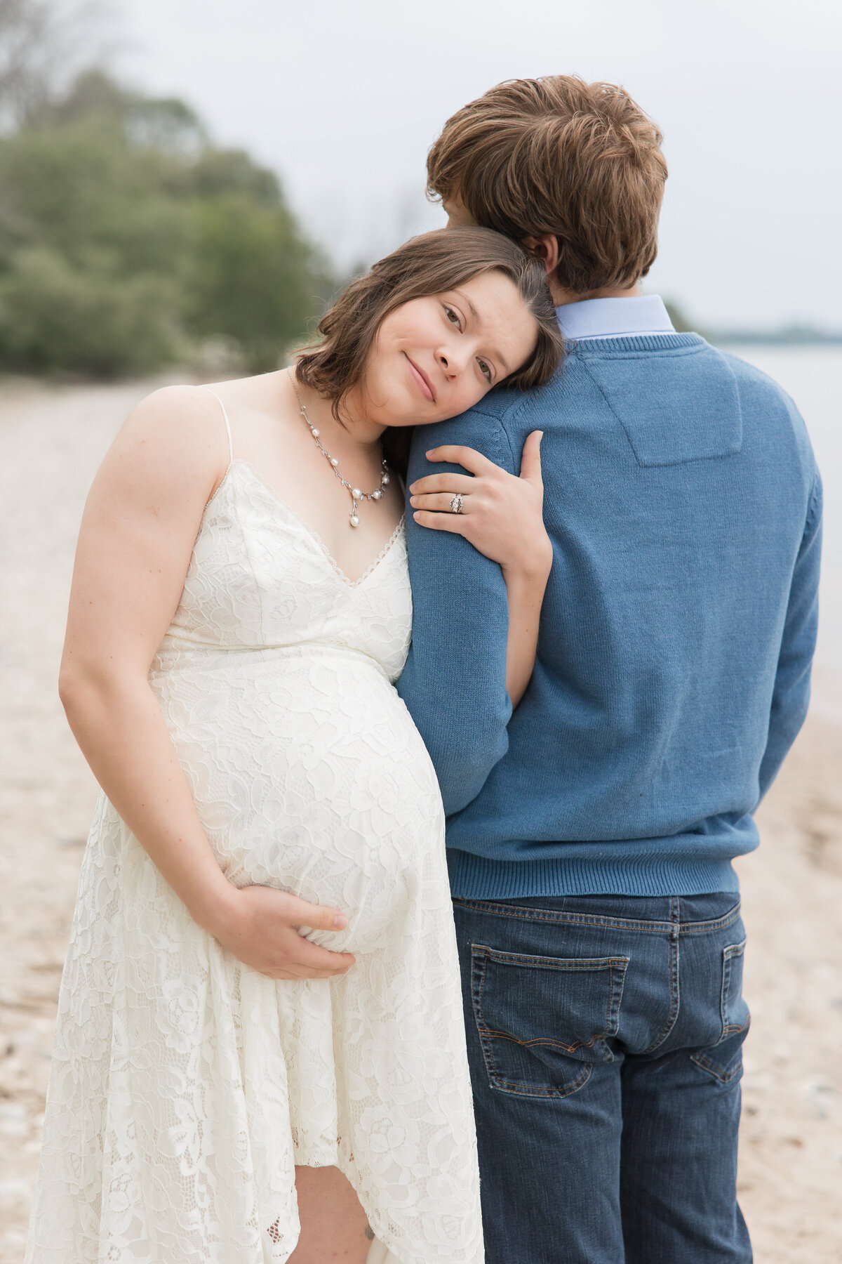 Expectant couple embracing on a beach with the mother looking at the camera