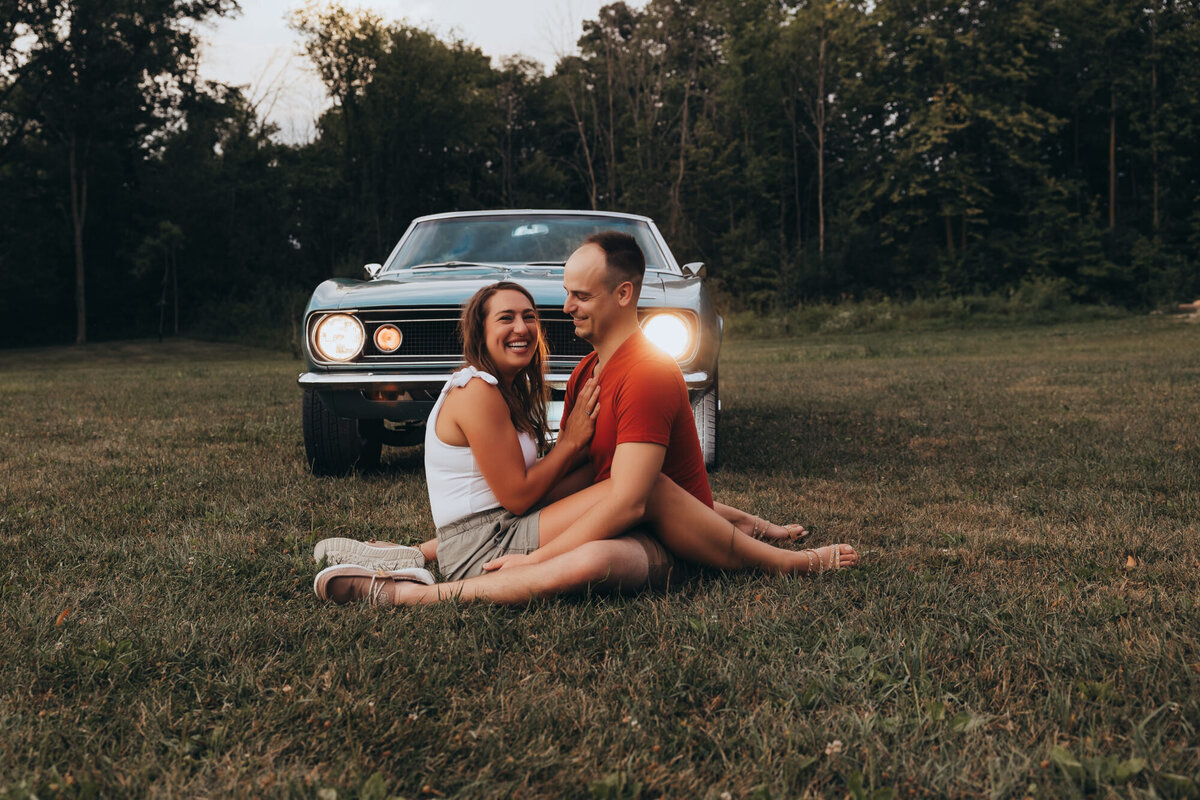 man and woman sit wrapped up in grass in front of classic 67 camaro