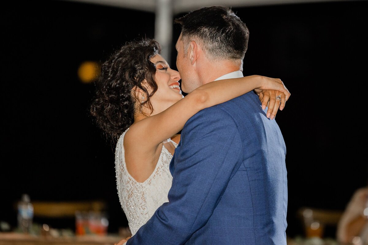 A joyful bride and groom sharing a dance at night during their Iowa wedding, the bride smiling as she rests her head on the groom’s shoulder.