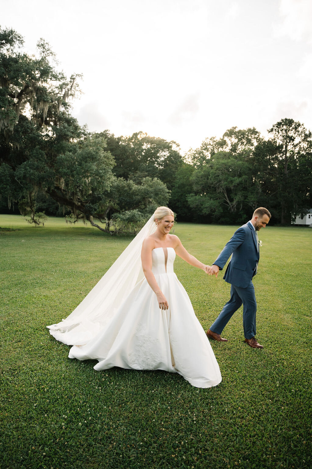 Bride and groom holding hands and laughing in open field