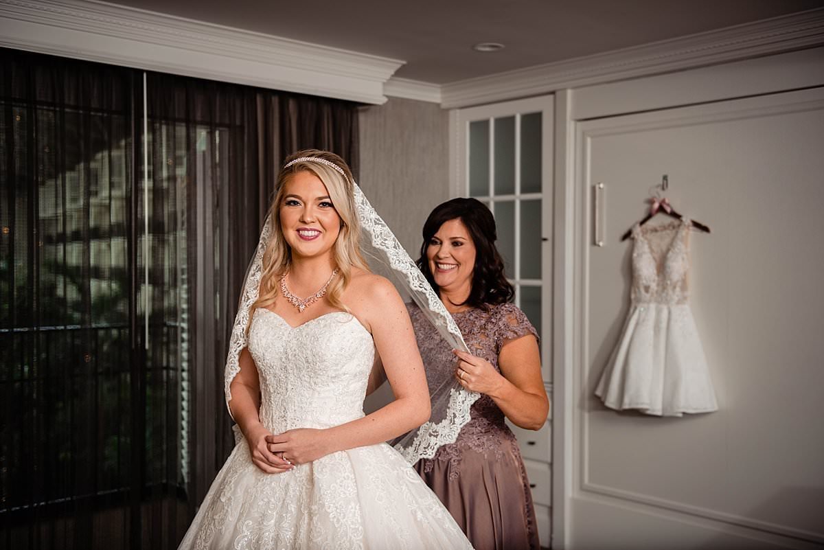 Mother of the bride helping her daughter put her lace trim veil