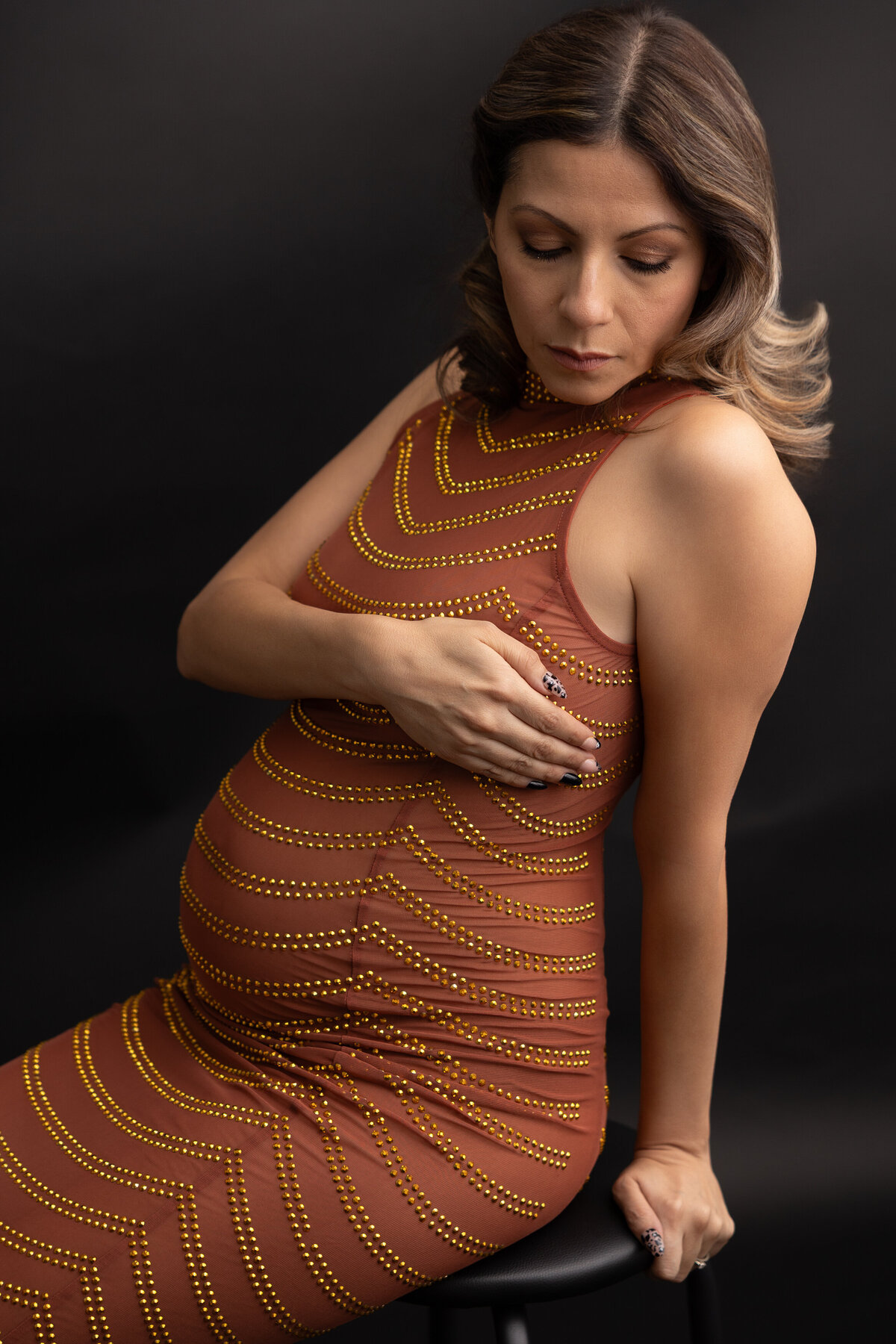 Pregnant mother wearing a glod-colored dress and sitting on a posing cube.