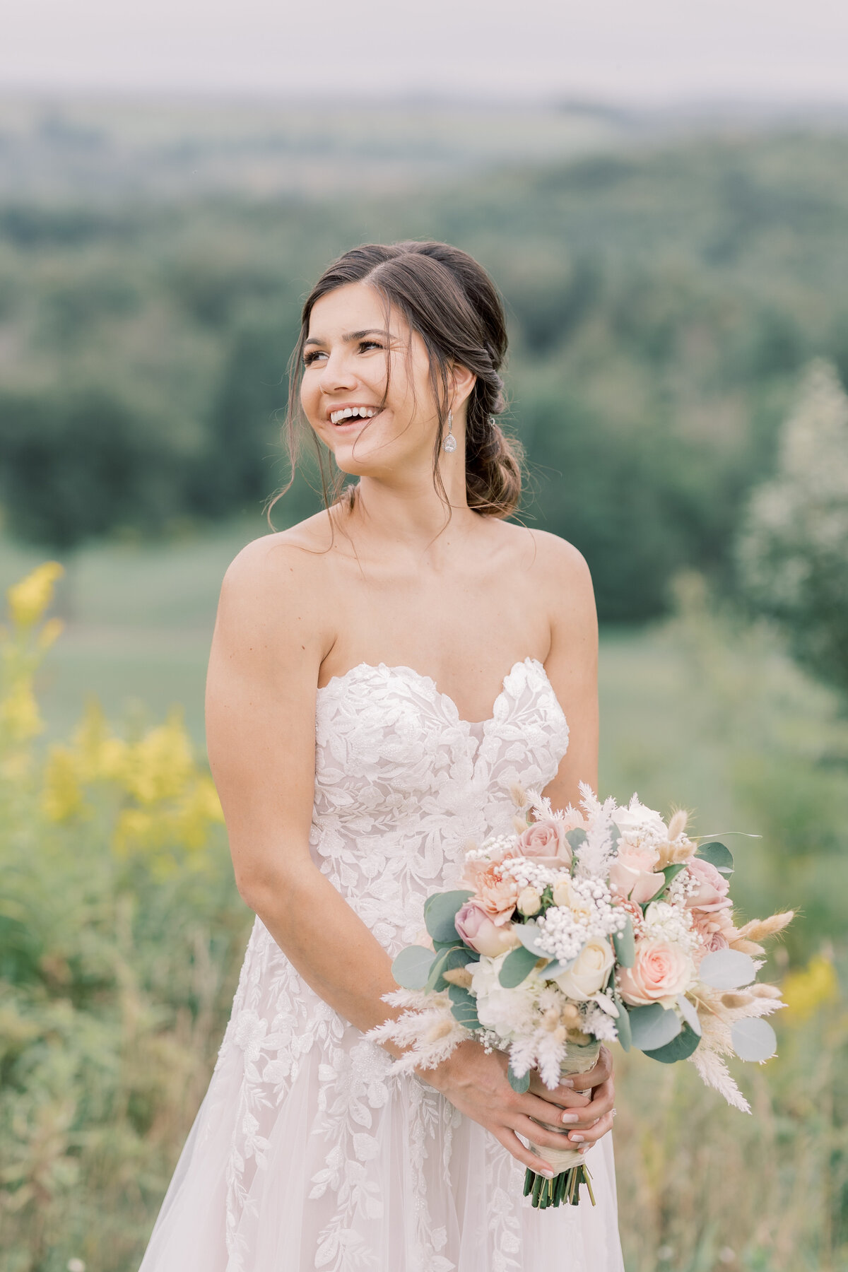 Bride smiling in a strapless wedding dress holding her bouquet with a mountain range behind her.