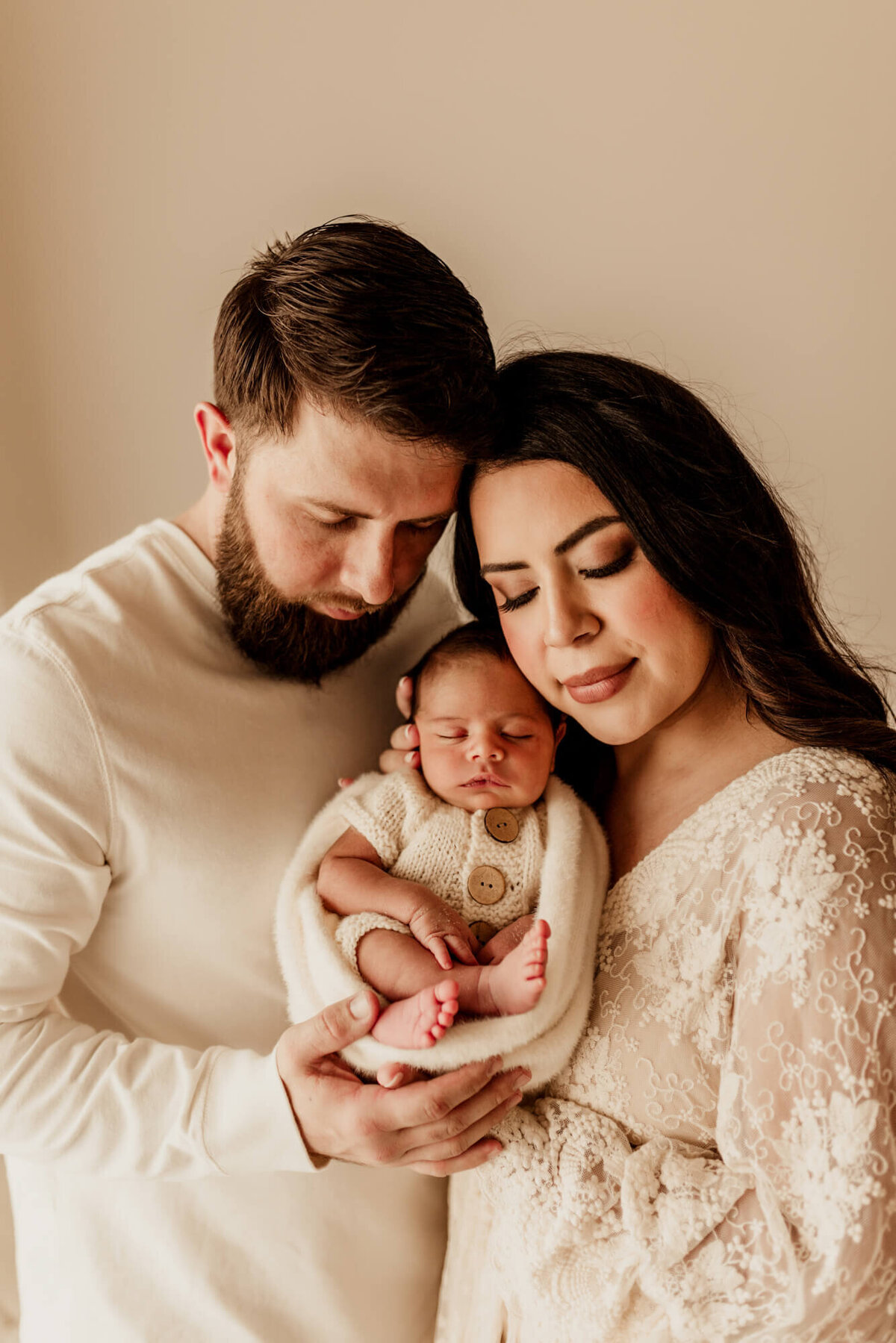 Family portrait of a mother wearing a lace dress and father weraing a cream shirt with their baby boy.