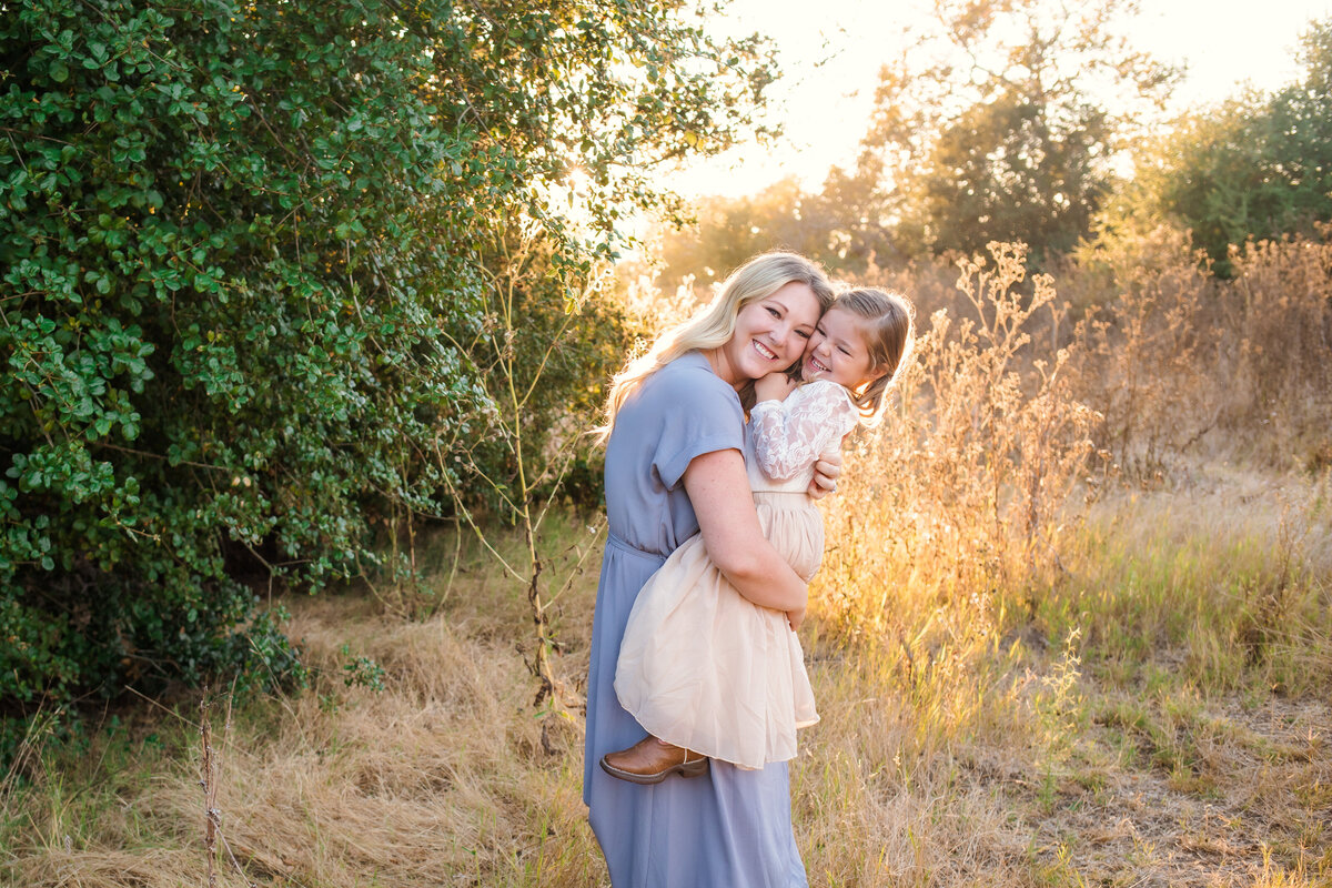 Family Photographer, a mother squeezes her daughter in a meadow