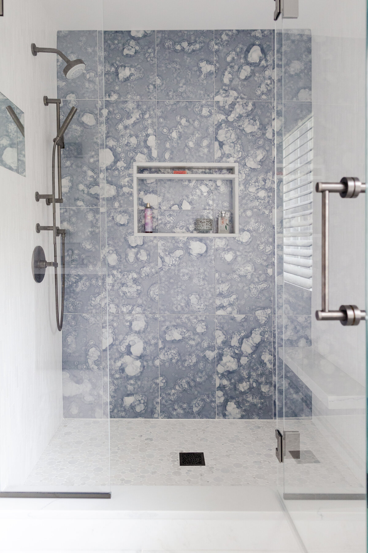 The walk-in shower features a blue water glass tile accent wall. The large format tiles have a frosted surface designed to resemble water-stained mirrors.