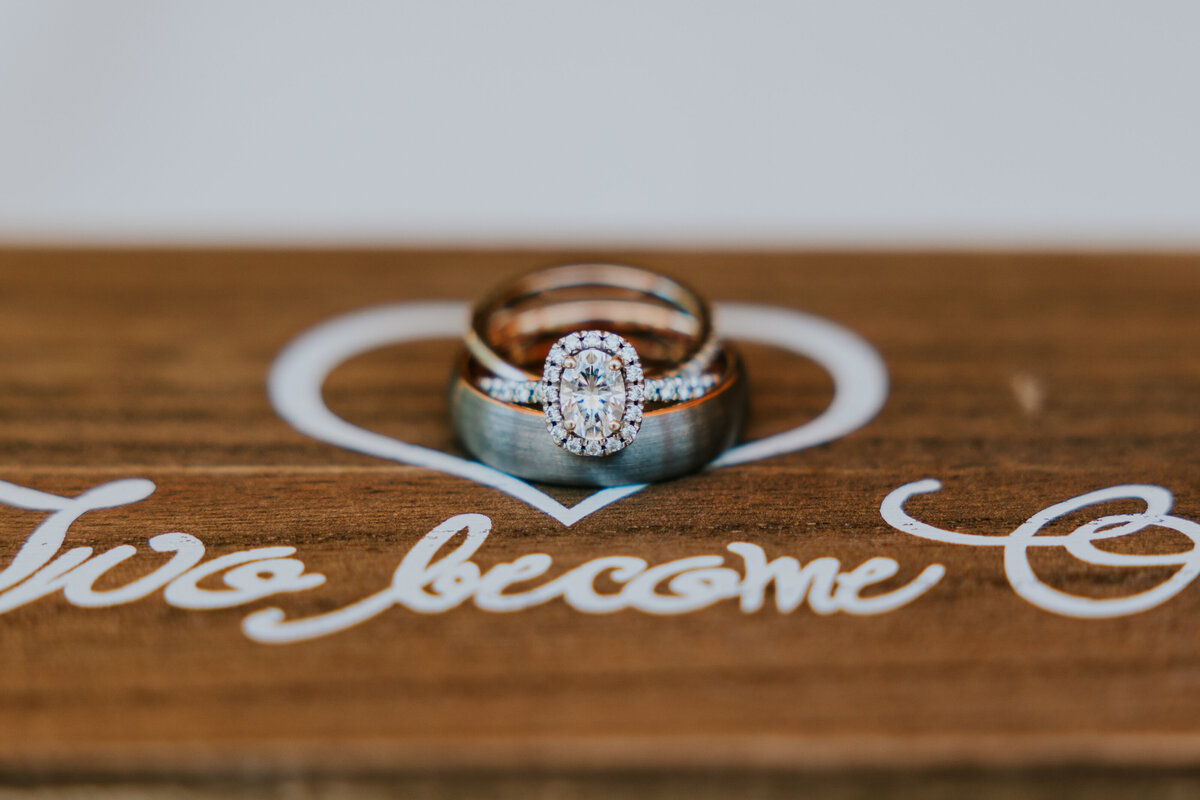 Wedding bands are stacked on top of wooden box that says "Two become one".