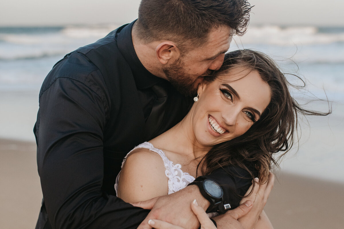 Bride and groom are holding each other on the beach.