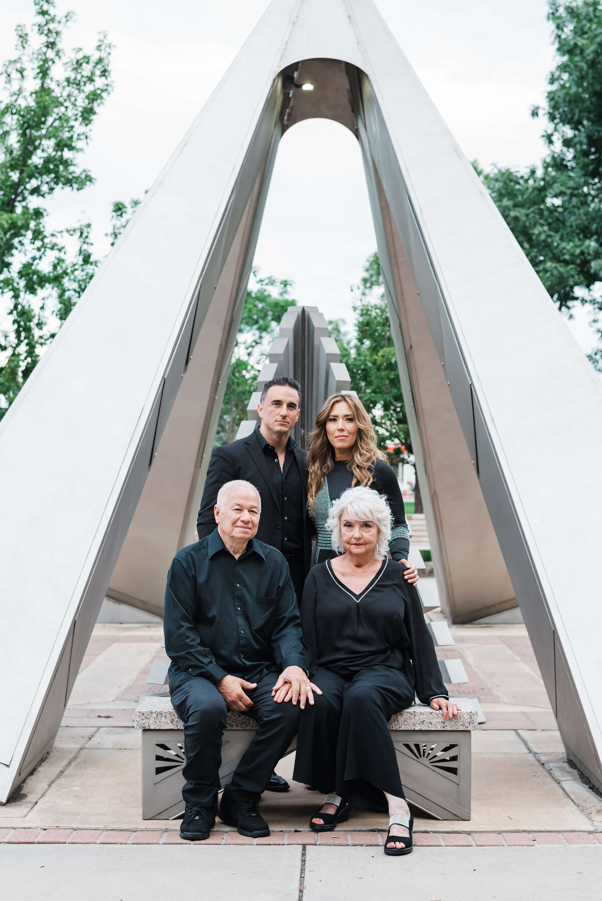 A set of grandparents and their daughter and son-in-law stand in front of an art sculpture and look into the camera