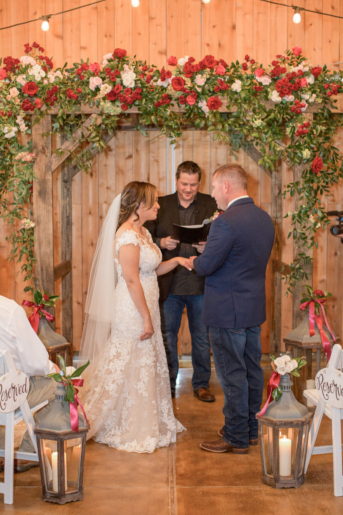 The groom places the ring on his brides finger, surrounded by an arch of red and white roses
