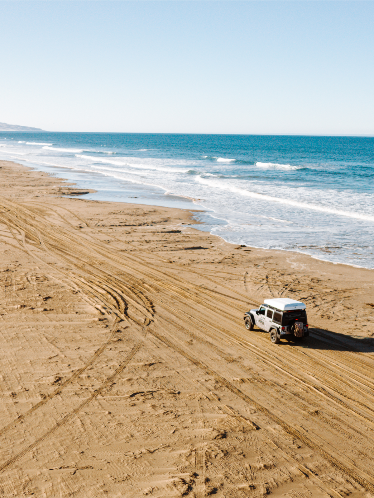 A Jeep driving along the sandy coastline of Pismo Beach, California, as part of a luxury overland road trip with stunning ocean views and off-road exploration