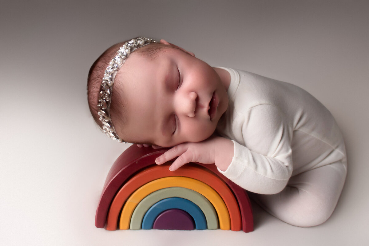 rainbow baby posing on a rainbow during her newborn session