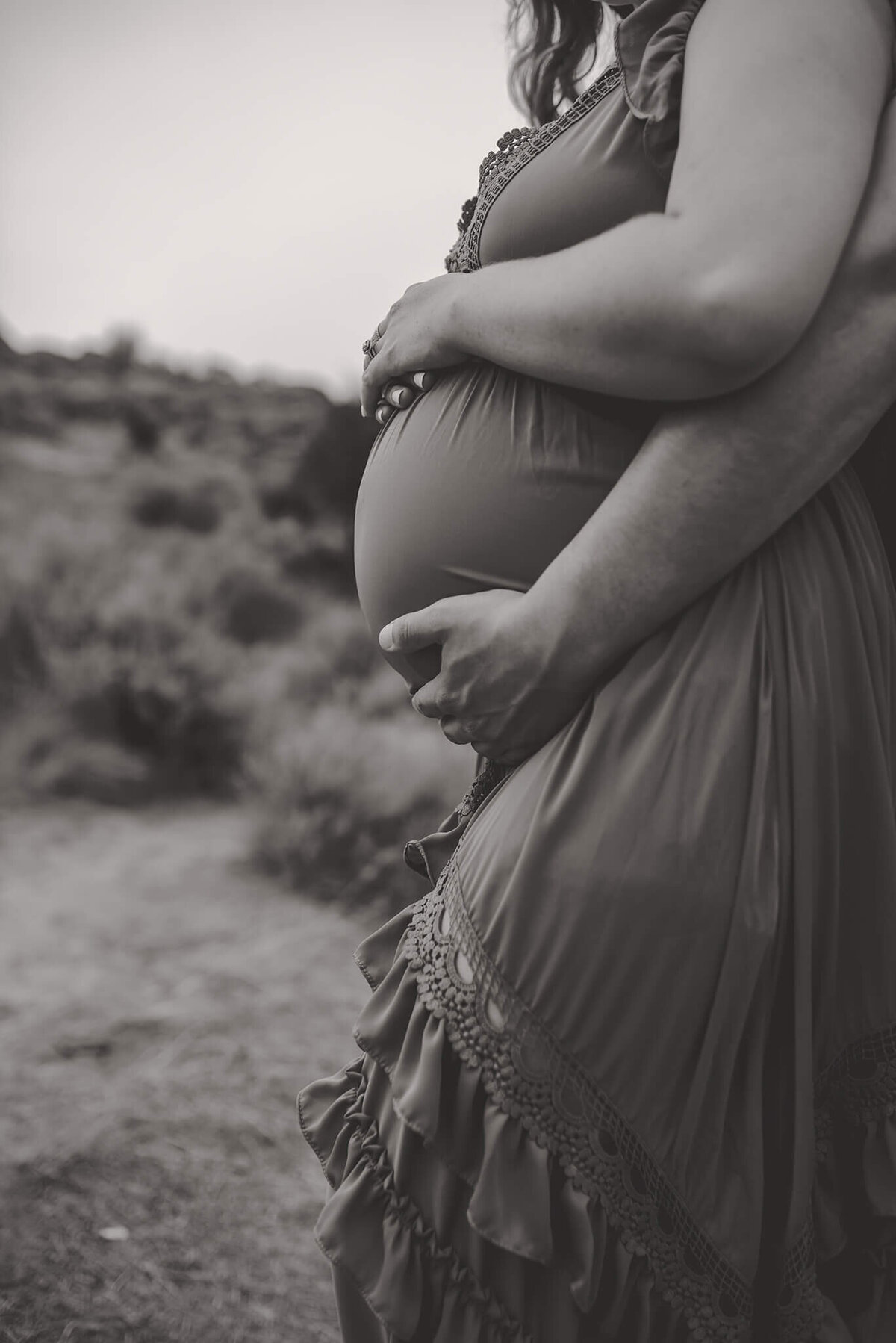 A close up black and white image of a man caressing his wife's pregnant belly from behind her. Portrait by Brittany Danielle
