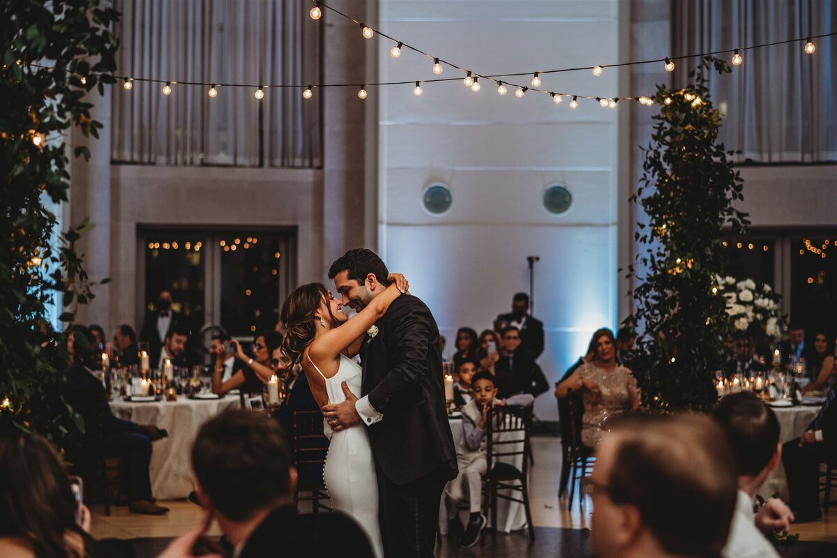 Baltimore wedding photographers captures first dance between bride and groom as they hold each other close on the dance floor with twinkle lights overhead