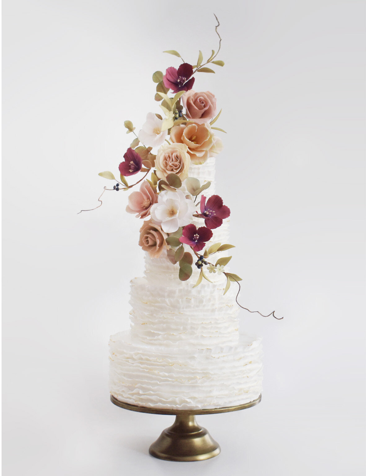 four tier white ruffled wedding cake with muted sugar flowers