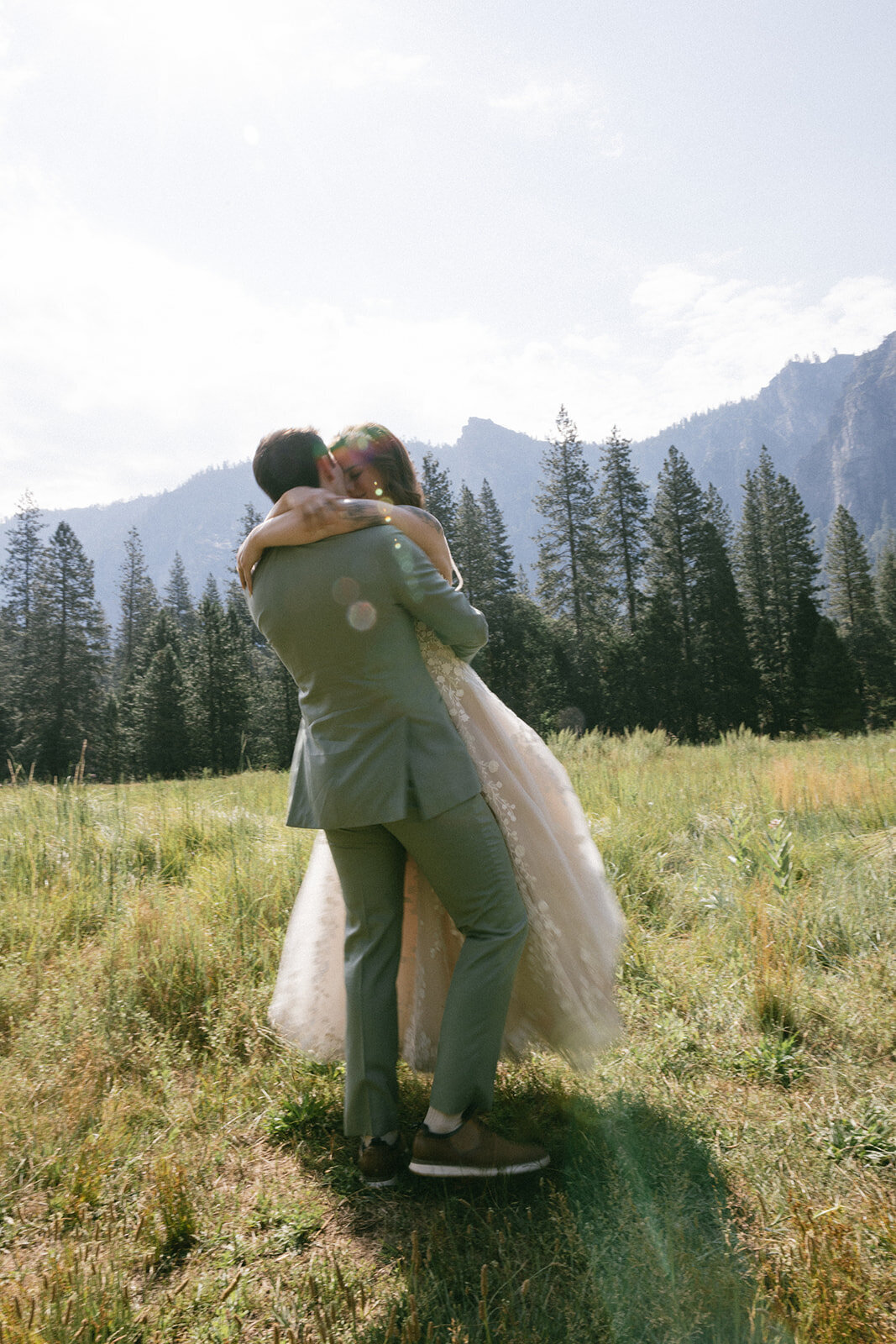 Couple twirls around on their elopement day at the El Capitan meadow surrounded by grass and pine trees.