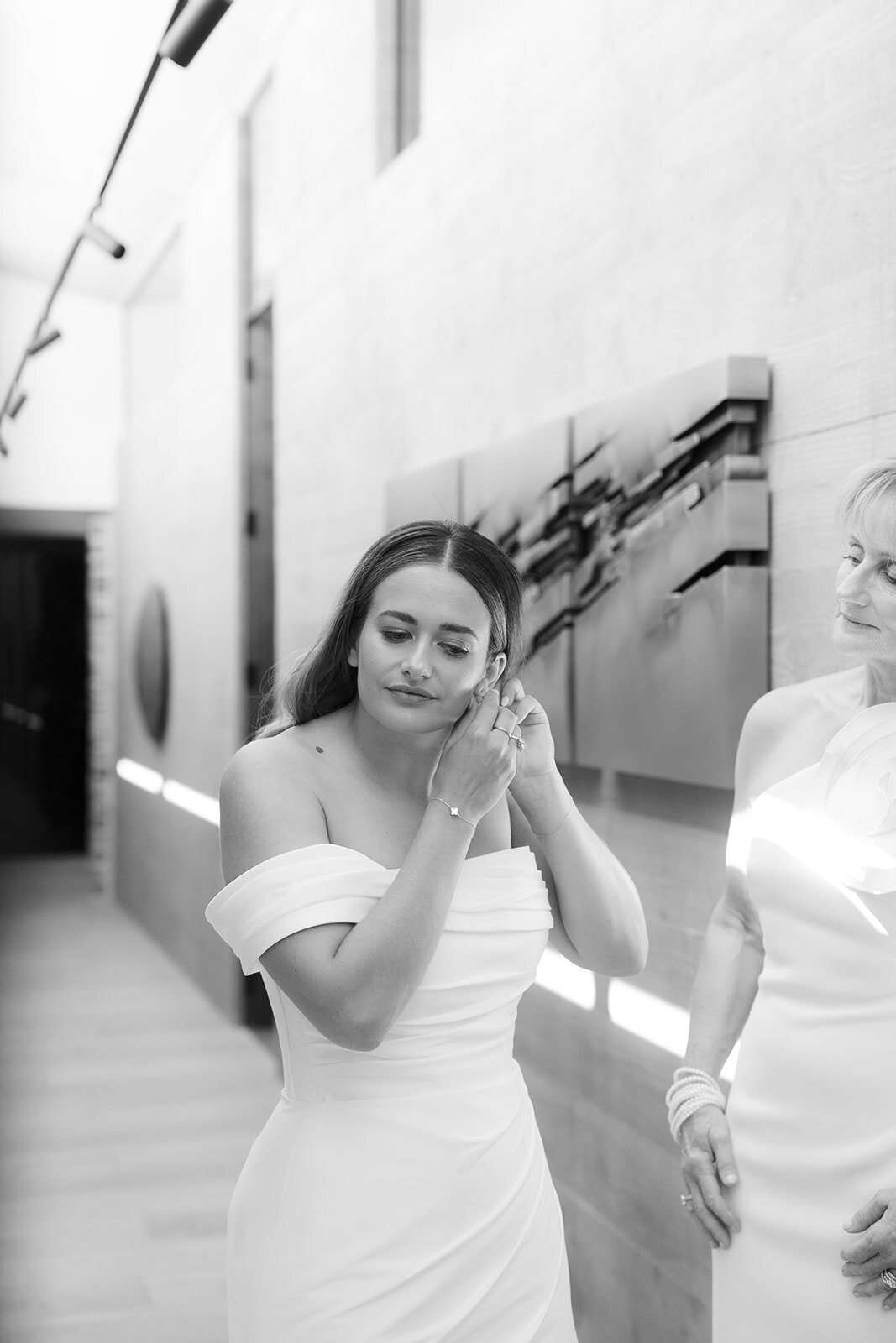 black and white image of bride putting jewellery on for wedding