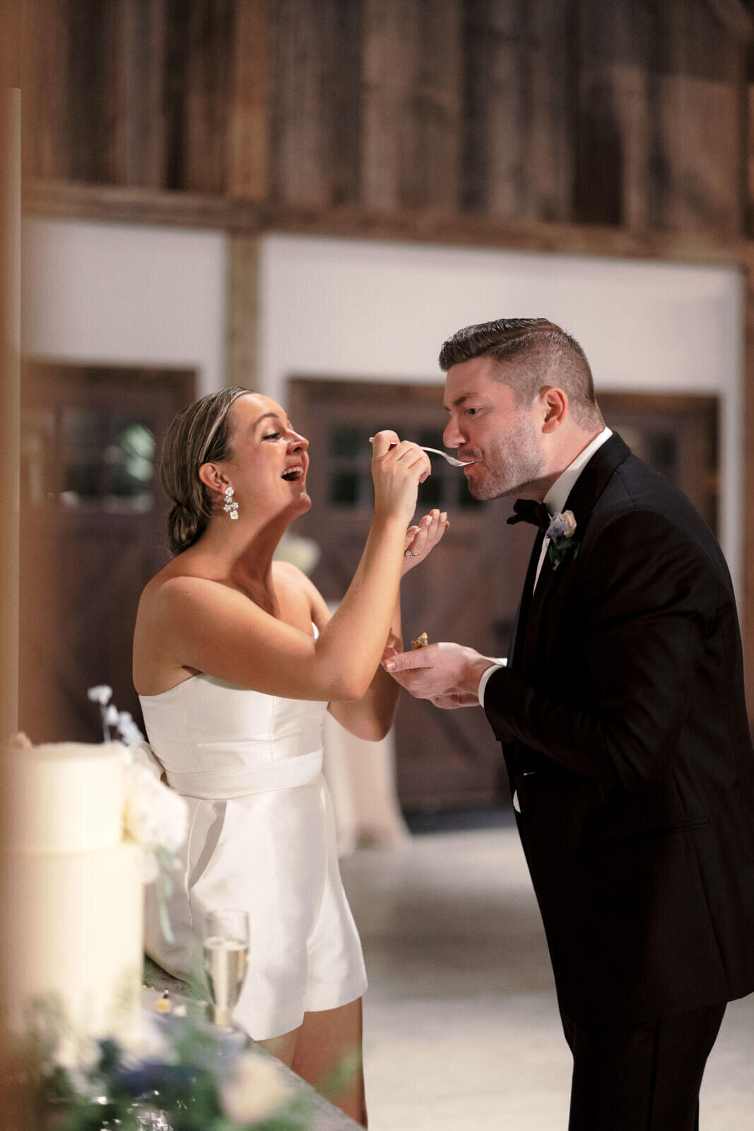 The bride is happily feeding a mouthful of cake to the groom at the wedding reception at Lion Rock Farm, CT. Image by Jenny Fu