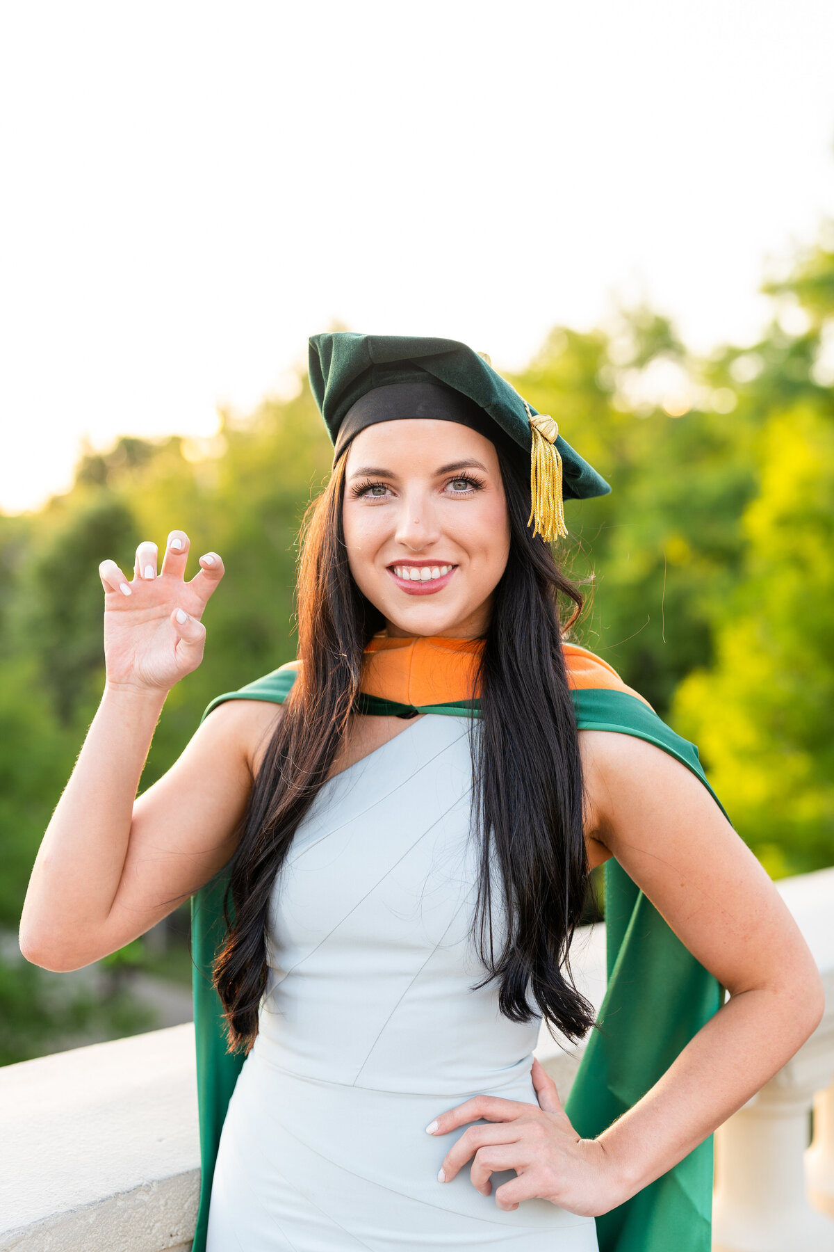 Baylor Doctoral Grad with college hand sign and doctoral hood and cap on a white bridge in Downtown Houston