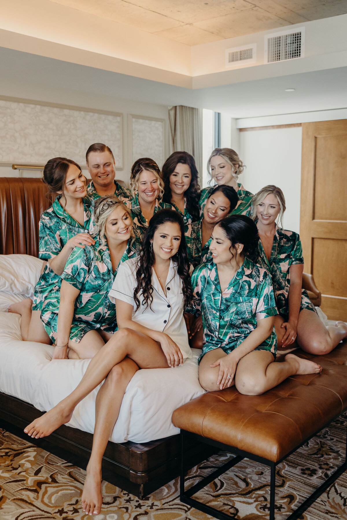 bride and bridesmaids having a fun moment on the bed in matching palm tree pajamas before getting dressed at the ben west palm