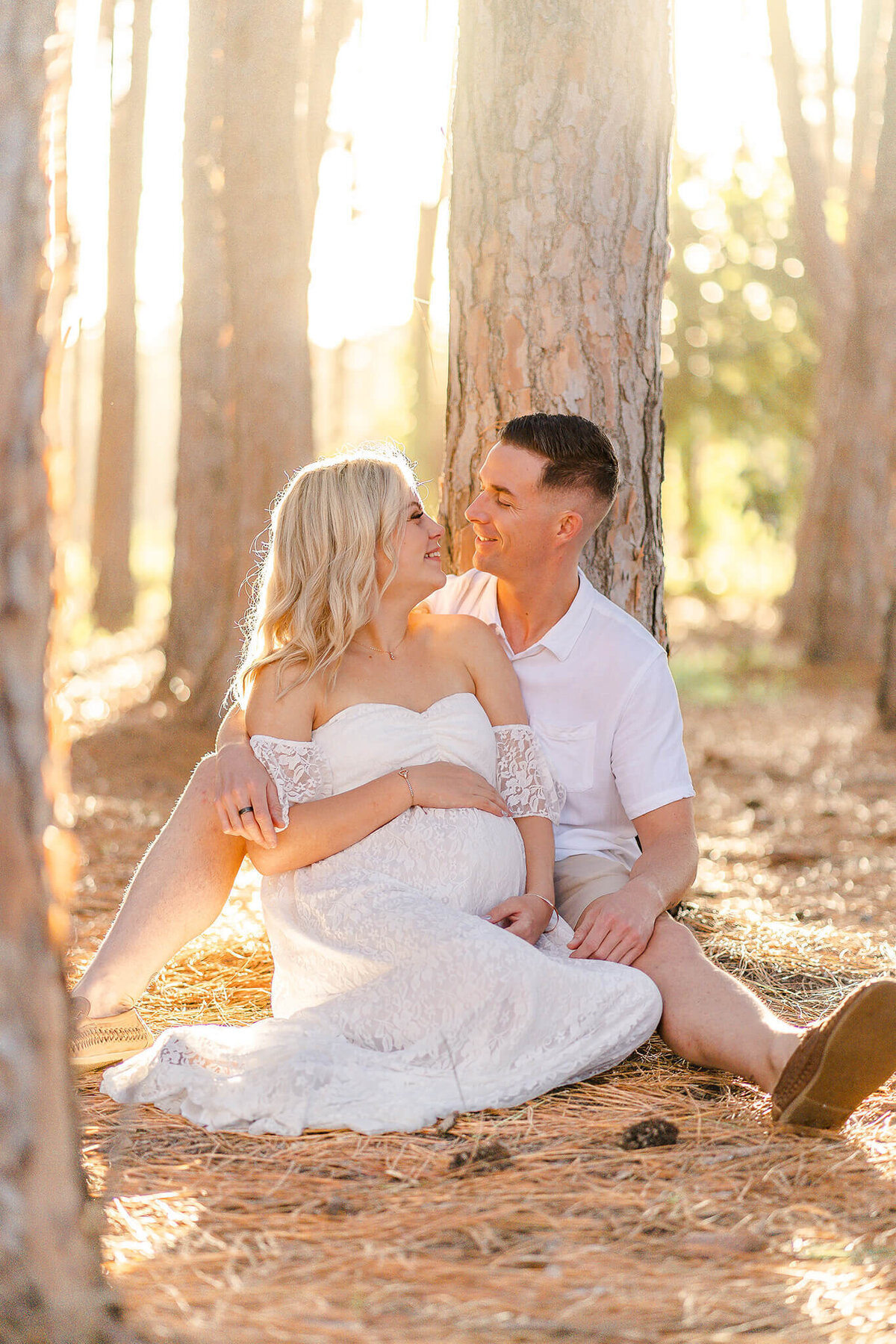 pregnant woman sitting next to husband during maternity shoot in pine forest in Gold Coast