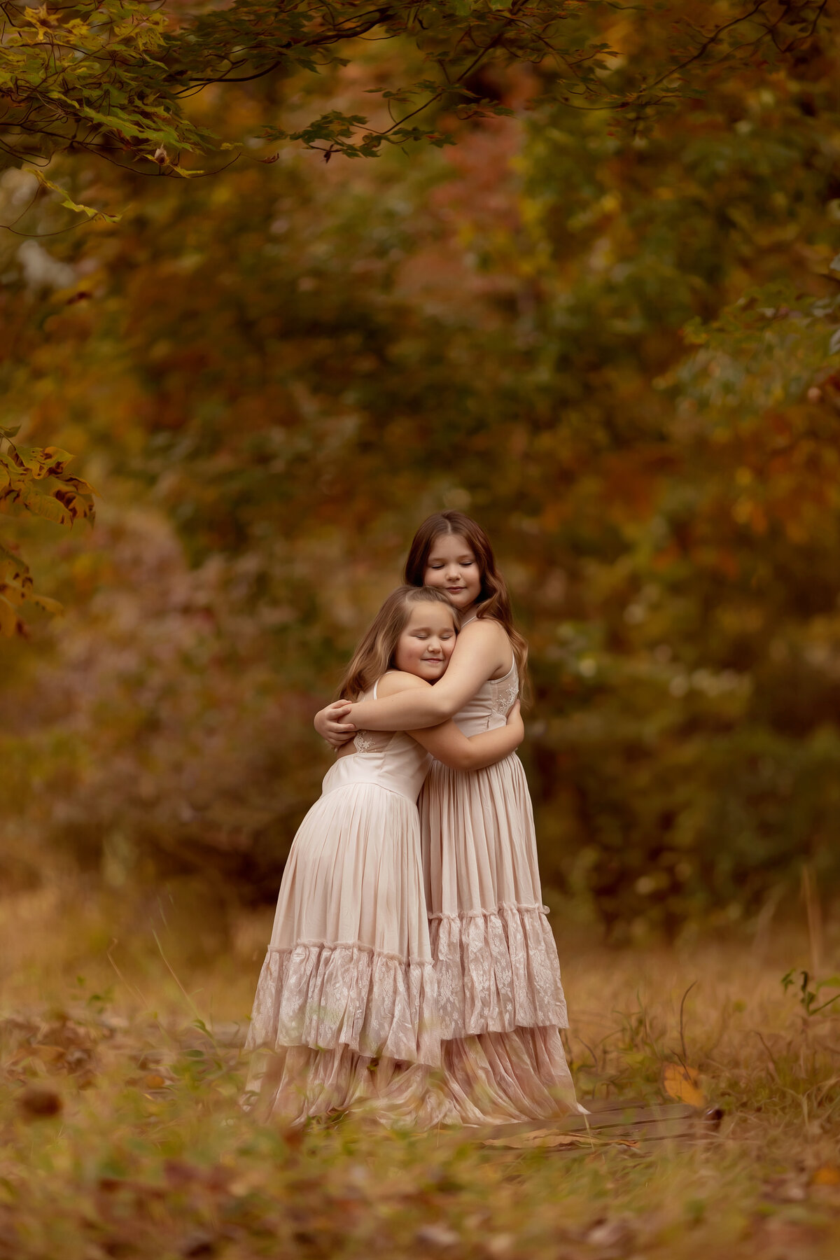 Two young sisters in matching pink dresses hug tightly in a forest trail for a New Jersey Family Photographer