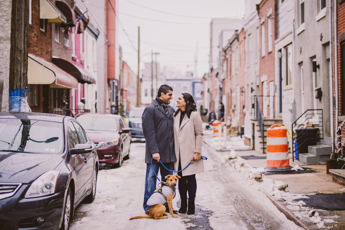 A couple standing in the middle of their neighborhood street with their puppy during their winter engagement session in philadelphia 